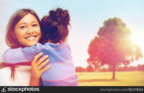 family, children and happy people concept - smiling mother and daughter hugging over oak tree at summer park background. happy mother and daughter hugging outdoors