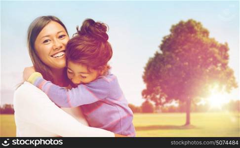 family, children and happy people concept - smiling mother and daughter hugging over oak tree at summer park background. happy mother and daughter hugging outdoors