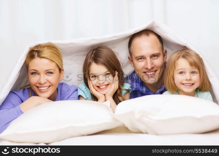 family, children and home concept - happy family with two kids under blanket at home