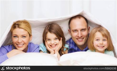 family, children and home concept - happy family with two kids under blanket at home