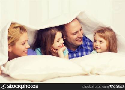 family, children and home concept - happy family with two kids under blanket at home