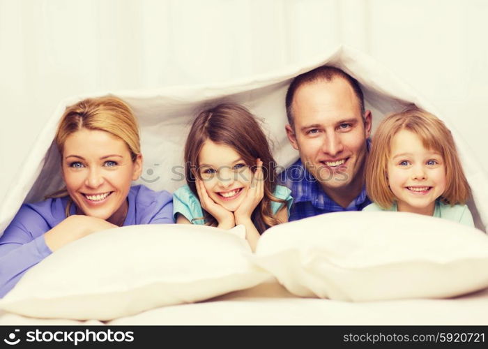 family, children and home concept - happy family with two kids under blanket at home