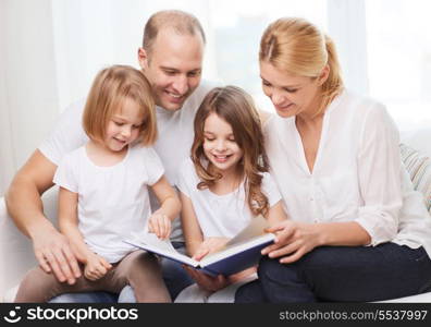 family, children and home concept - smiling family and two little girls with book at home