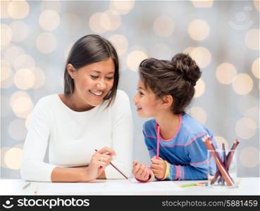 family, children and people concept - happy mother and daughter drawing over holidays lights background