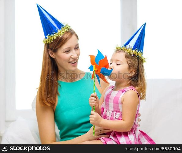 family, children, celebration and happy people concept - happy mother and daughter in blue hats with pinwheel