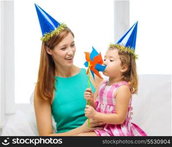 family, children, celebration and happy people concept - happy mother and daughter in blue hats with pinwheel