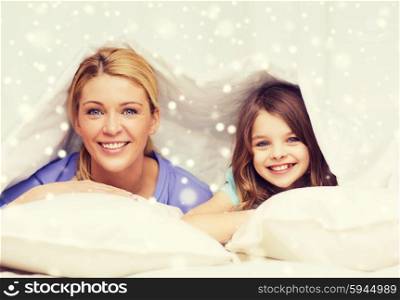 family, children, comfort, bedding and home concept - happy mother and girl under blanket over snowflakes background