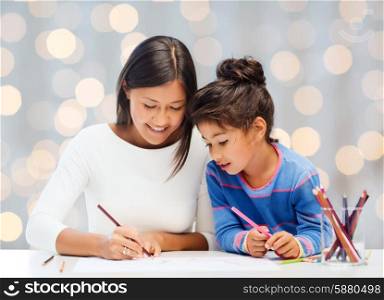 family, children, creativity and happy people concept - happy mother and daughter drawing with pencils over holidays lights background