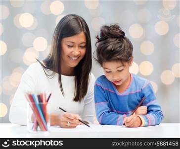 family, children, creativity and happy people concept - happy mother and daughter drawing with pencils over holidays lights background