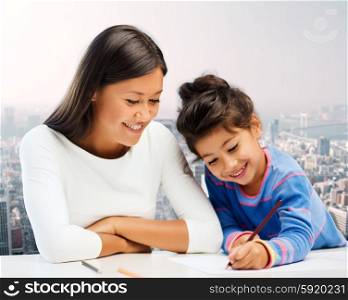 family, children, creativity and happy people concept - happy mother and daughter drawing with pencils over city background