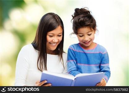 family, children, education and happy people concept - happy mother and little daughter reading book over green background