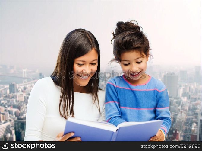 family, children, education and happy people concept - happy mother and little daughter reading book over city background