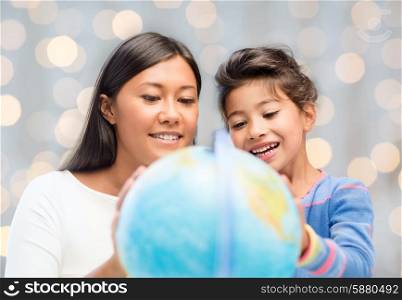 family, children, education, geography and people concept - happy mother and daughter with globe over holidays lights background
