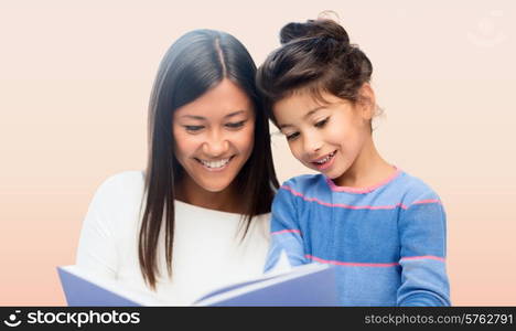 family, children, education, school and happy people concept - happy mother and daughter reading book over pink background