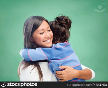 family, children, education, school and happy people concept - happy mother or teacher and little girl hugging over green chalk board background