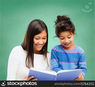 family, children, education, school and happy people concept - happy teacher and little girl reading book over green chalk board background