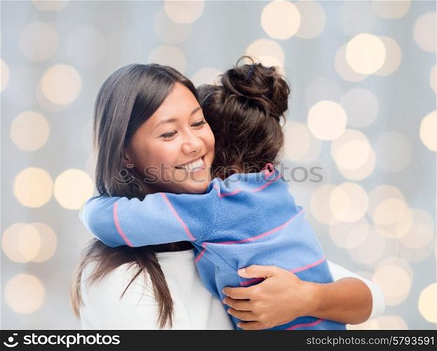 family, children, love and happy people concept - happy mother and daughter hugging over holidays lights background