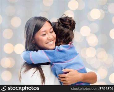 family, children, love and happy people concept - happy mother and daughter hugging over holidays lights background