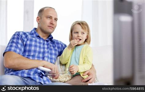 family, children, parenthood people concept - happy father and daughter eating popcorn and watching tv at home