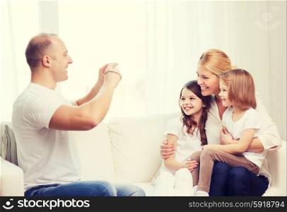 family, children, photography and home concept - smiling happy father taking picture of mother and two daughters at home