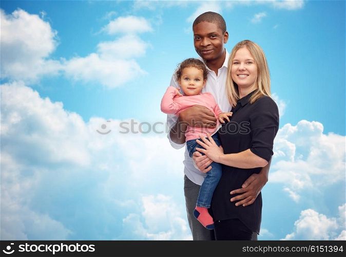 family, children, race and nationality concept - happy multiracial mother, father and little child over blue sky and clouds background