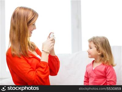 family, children, technology and happy people concept - smiling mother taking picture of daughter with digital camera