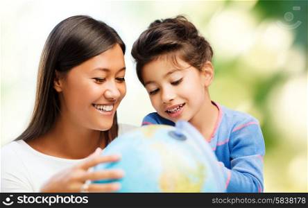 family, children, travel, geography and happy people concept - mother and daughter with globe over green background