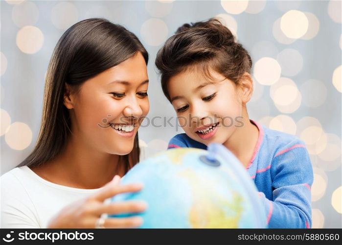 family, children, travel, geography and happy people concept - mother and daughter with globe over holidays lights background