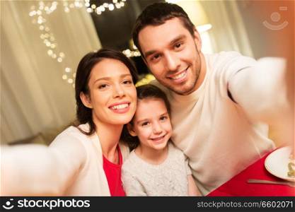 family, christmas and holidays concept - happy mother, father and little daughter taking selfie at home. happy family taking selfie at christmas