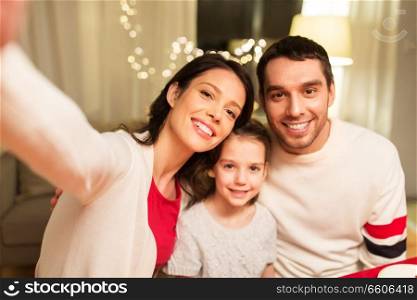 family, christmas and holidays concept - happy mother, father and little daughter taking selfie at home. happy family taking selfie at christmas
