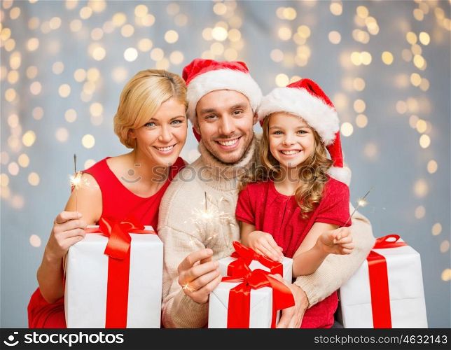 family, christmas and people concept - happy family in santa helper hats with many gift boxes and sparklers over lights background