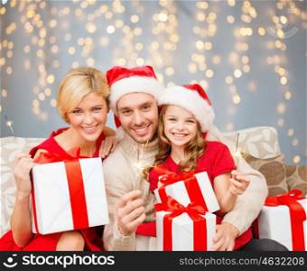 family, christmas and people concept - happy family in santa helper hats with many gift boxes and sparklers over lights background