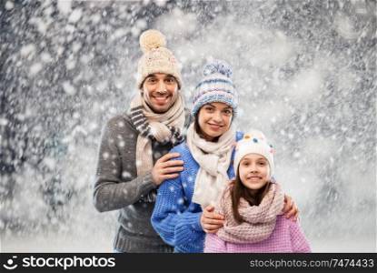 family, christmas and winter clothes concept - happy mother, father and little daughter in knitted hats and scarves over snow background. happy family in winter clothes on snow background