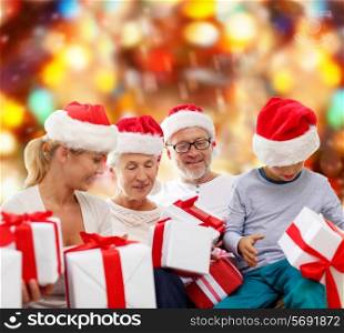 family, christmas, generation, holidays and people concept - happy family in santa helper hats with gift boxes sitting over red lights background