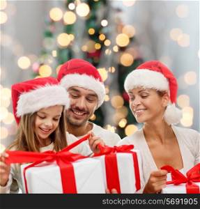 family, christmas, generation, holidays and people concept - happy family in santa helper hats with gift boxes sitting over christmas tree lights background