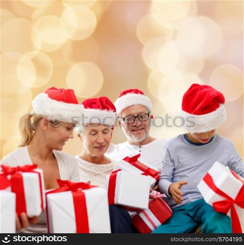 family, christmas, generation, holidays and people concept - happy family in santa helper hats with gift boxes sitting over beige lights background