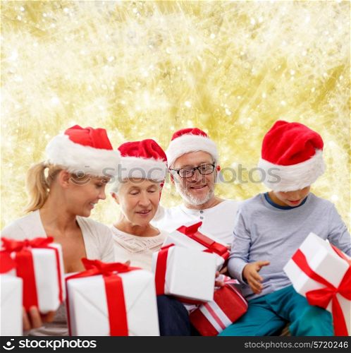 family, christmas, generation, holidays and people concept - happy family in santa helper hats with gift boxes sitting over yellow lights background