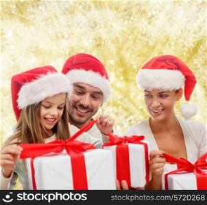 family, christmas, generation, holidays and people concept - happy family in santa helper hats with gift boxes over yellow lights background