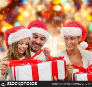 family, christmas, generation, holidays and people concept - happy family in santa helper hats with gift boxes over red lights background