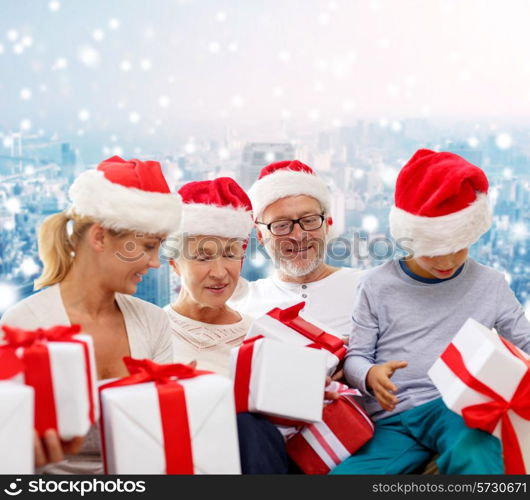 family, christmas, generation, holidays and people concept - happy family in santa helper hats with gift boxes sitting over blue snowy background