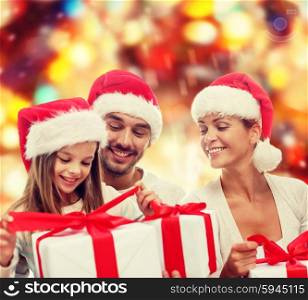 family, christmas, generation, holidays and people concept - happy family in santa helper hats with gift boxes sitting over red lights background