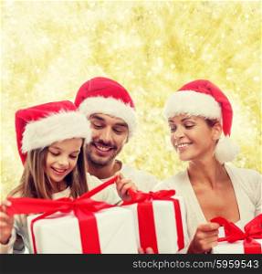 family, christmas, generation, holidays and people concept - happy family in santa helper hats with gift boxes sitting over yellow lights background