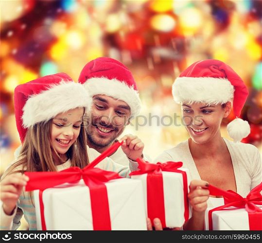family, christmas, generation, holidays and people concept - happy family in santa helper hats with gift boxes over red lights background