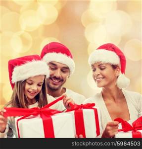 family, christmas, generation, holidays and people concept - happy family in santa helper hats with gift boxes sitting over beige lights background