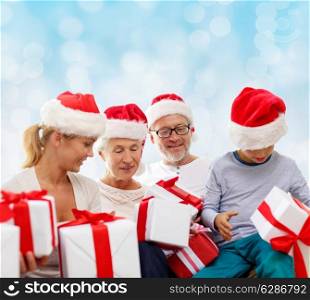 family, christmas, generation, holidays and people concept - happy family in santa helper hats with gift boxes sitting over blue lights background