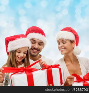 family, christmas, generation, holidays and people concept - happy family in santa helper hats with gift boxes sitting over blue lights background