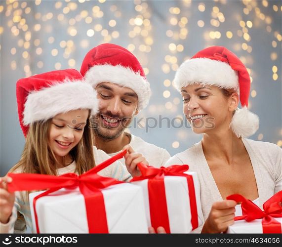family, christmas, holidays and people concept - happy family in santa helper hats with gift boxes over lights background
