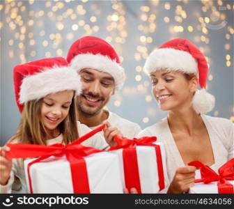 family, christmas, holidays and people concept - happy family in santa helper hats with gift boxes over lights background