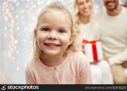 family, christmas, holidays and people concept - happy little girl with mother father over lights background. happy little girl with family at christmas