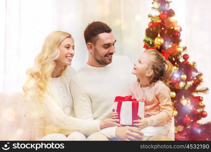 family, christmas, holidays and people concept - happy mother, father and little daughter with gift box sitting on sofa at home over lights